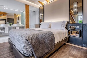 A modern hotel room with a large bed, a bathroom with a vanity, and a staircase.