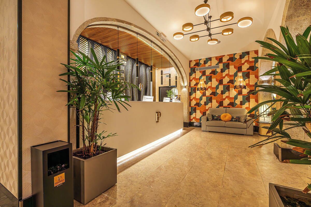 Un vestíbulo con mostrador de recepción, un sofá, plantas en macetas y una pared con diseño.