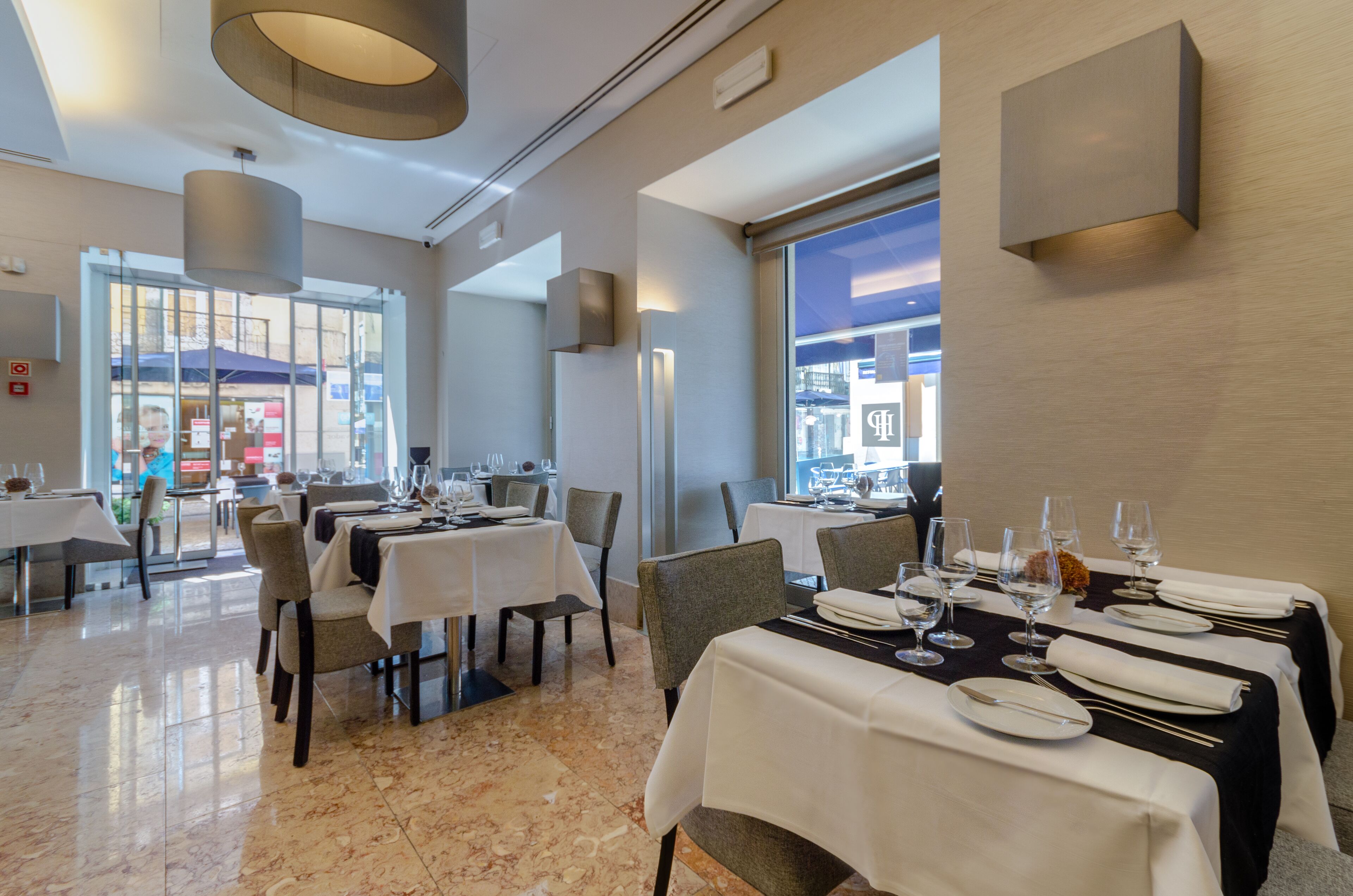 Un restaurante con mesas dispuestas para comer, ventanas amplias y un interior moderno y cuidado.