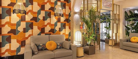 A lobby with a patterned wall, a sofa with a yellow pillow, a lamp, and a sign that reads 'Drink & Dine.'