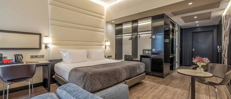 Une chambre d’hôtel moderne, équipée d’un lit, d’un bureau, d’une chaise, d’un canapé et d’une petite table sur laquelle est posé un vase de fleurs.