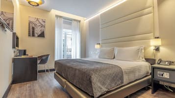 A modern hotel room with a large bed, bedside table, and a desk with a chair.