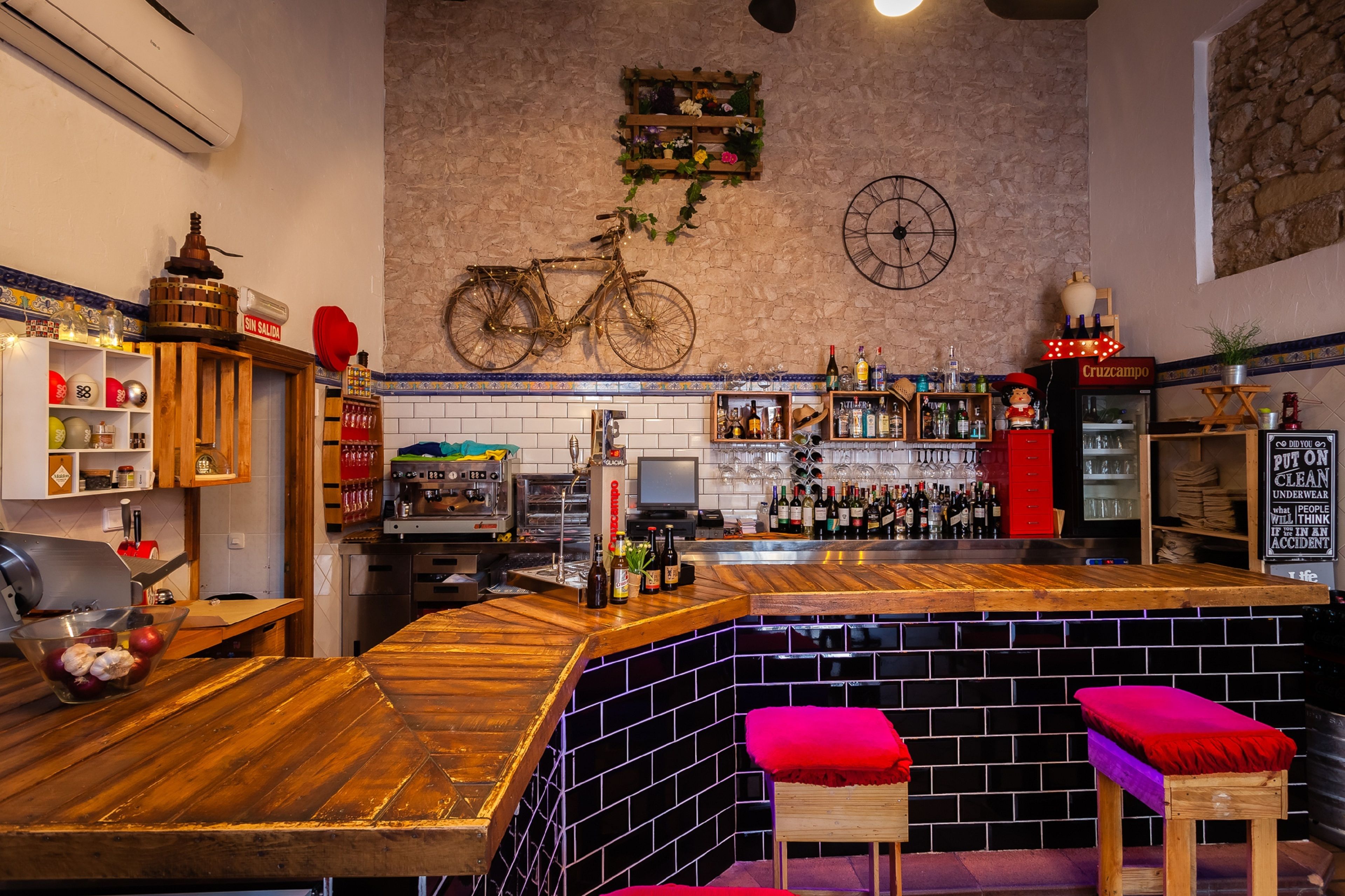 A bar area with a wooden counter, stools, and a variety of bottles.