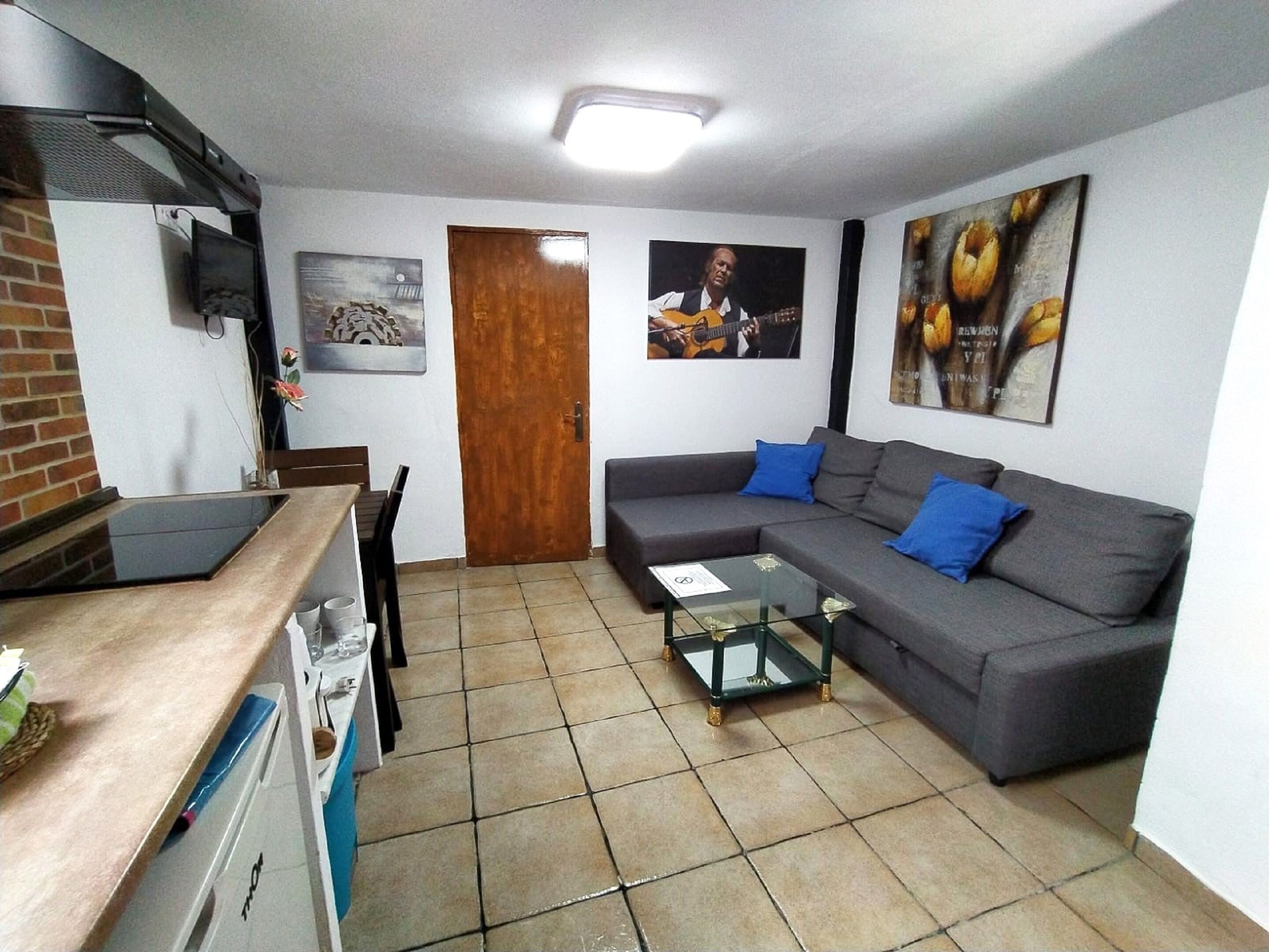 Un espace de vie compact comprenant un coin cuisine, un canapé, une table basse en verre et un coin repas.