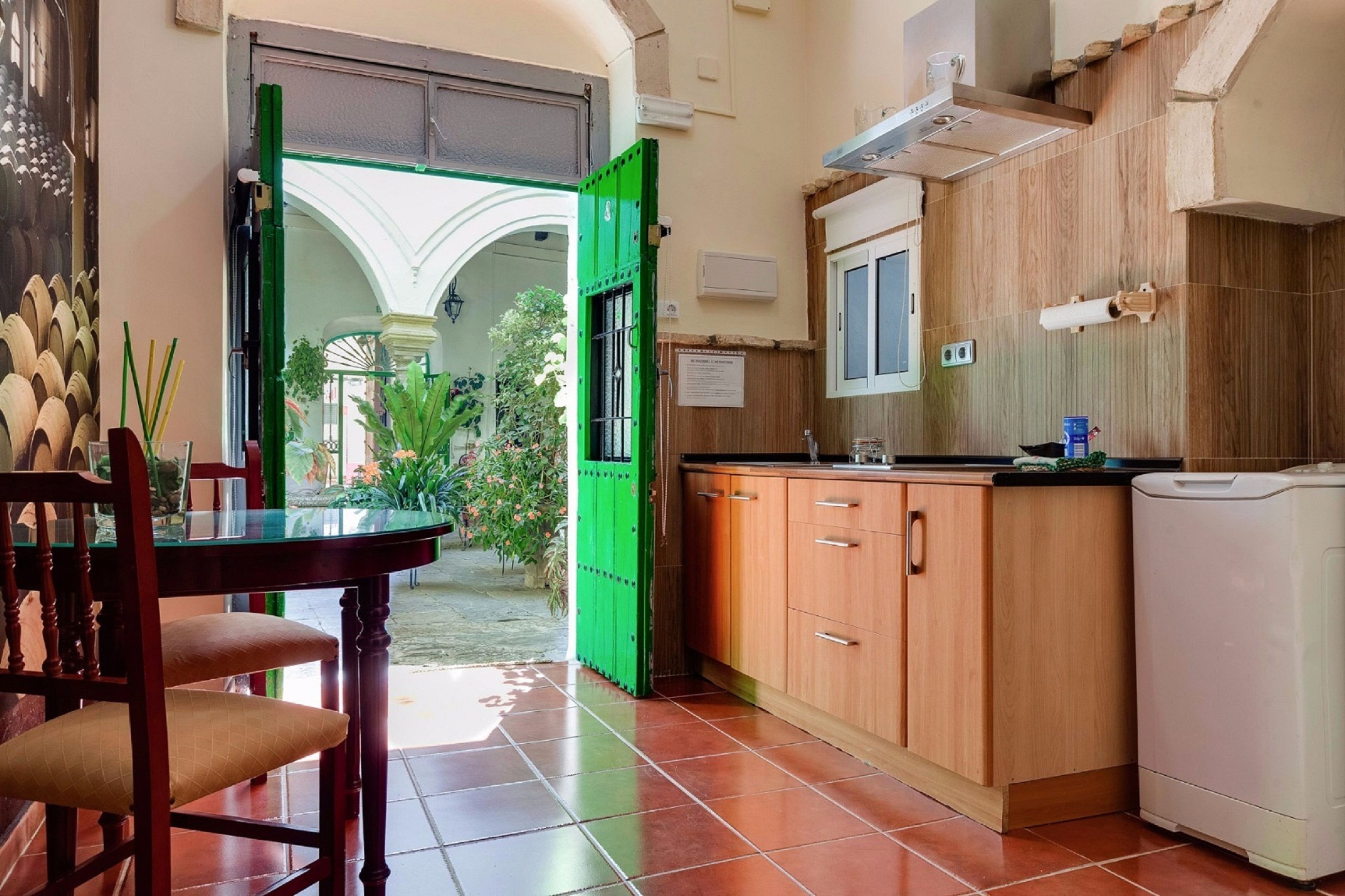 A kitchen with wooden cabinets, a white washing machine, and a green door leading to an outdoor area with plants.