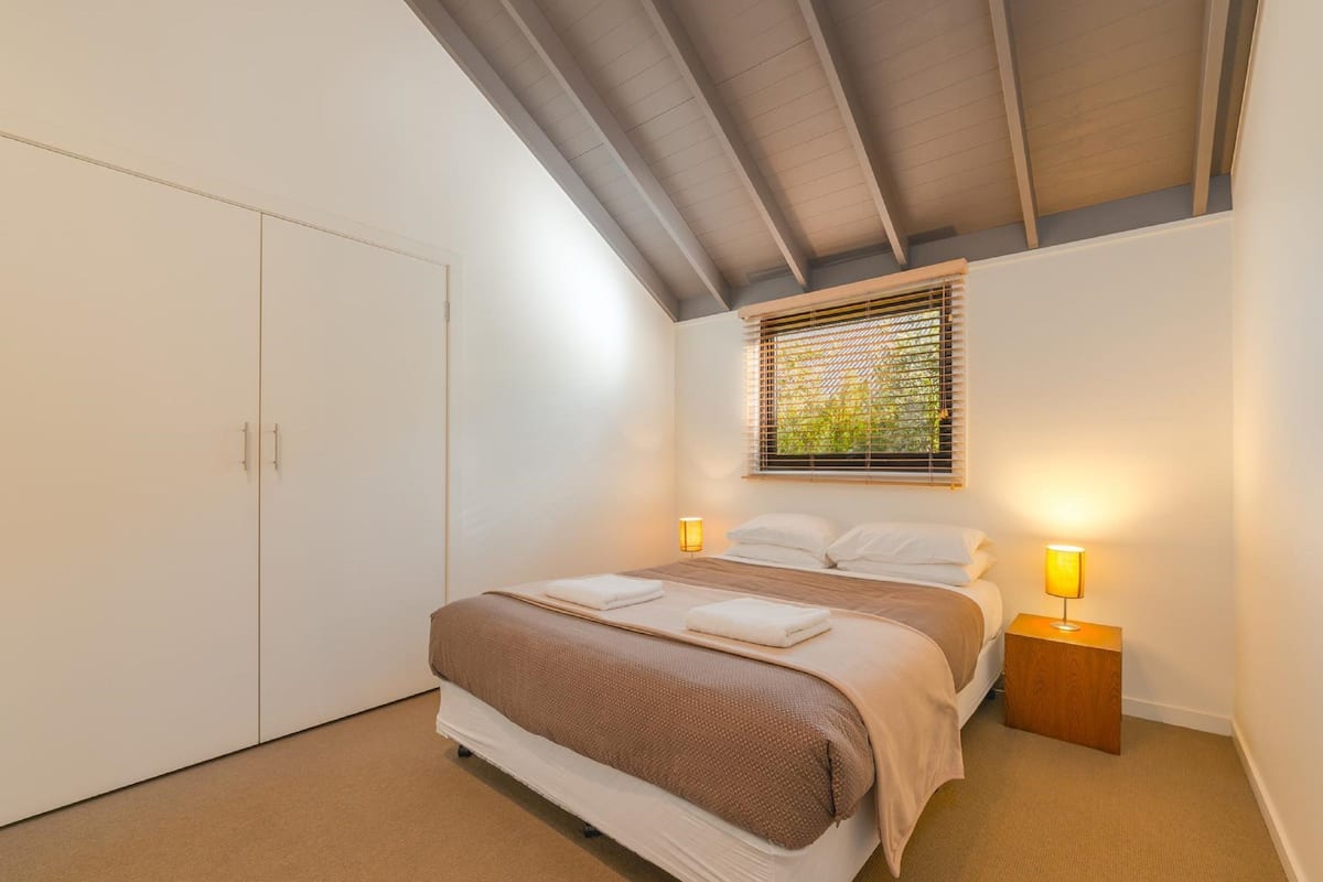 Un dormitorio con cama, lámparas de noche, una ventana con persianas y un armario.