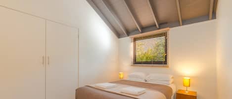 Un dormitorio con cama, lámparas de noche, una ventana con persianas y un armario.