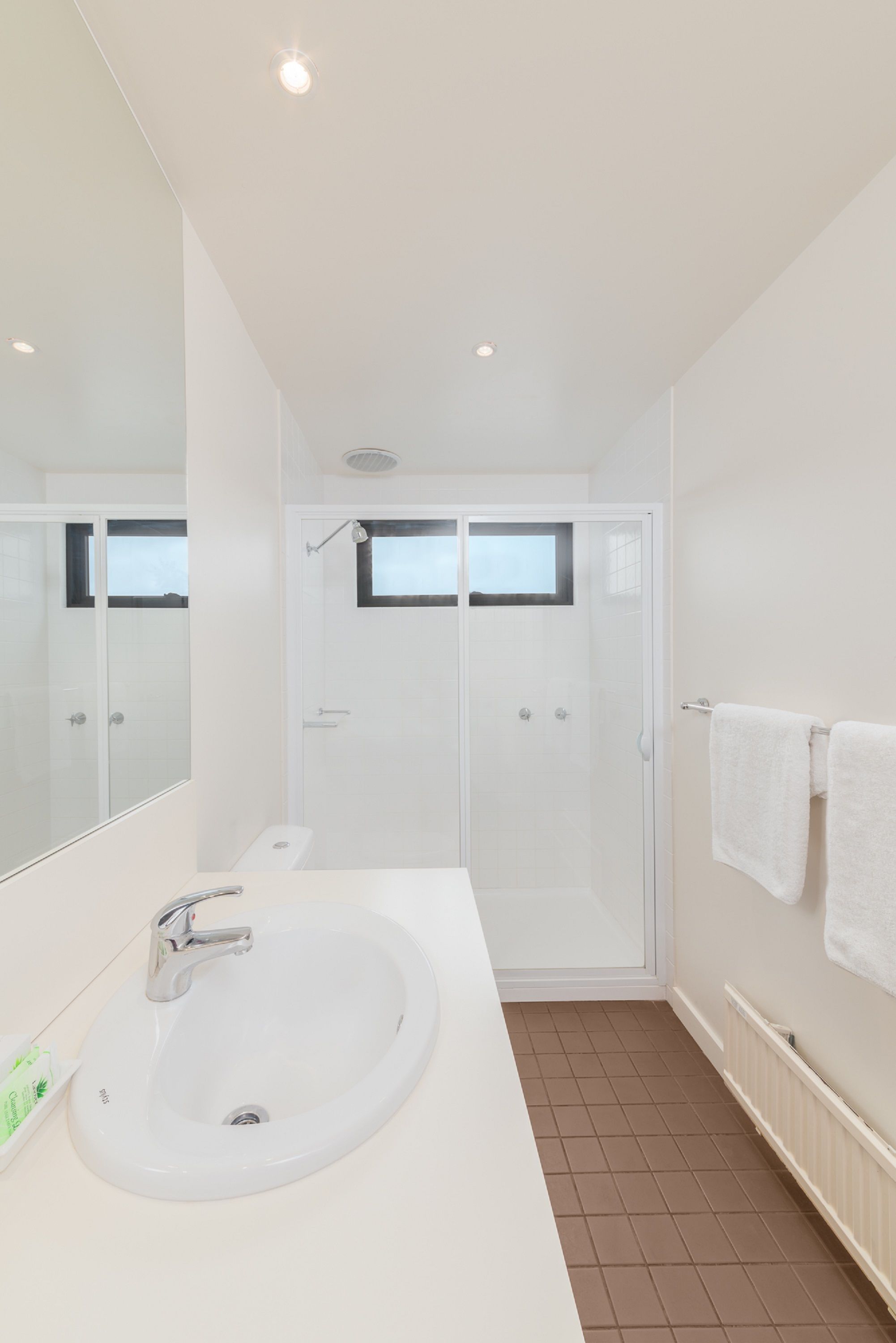 A modern bathroom with a white sink, a glass-enclosed shower, and a large mirror.