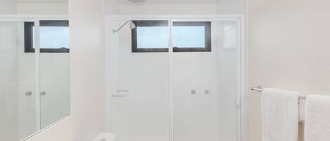A modern bathroom with a white sink, a glass-enclosed shower, and a large mirror.