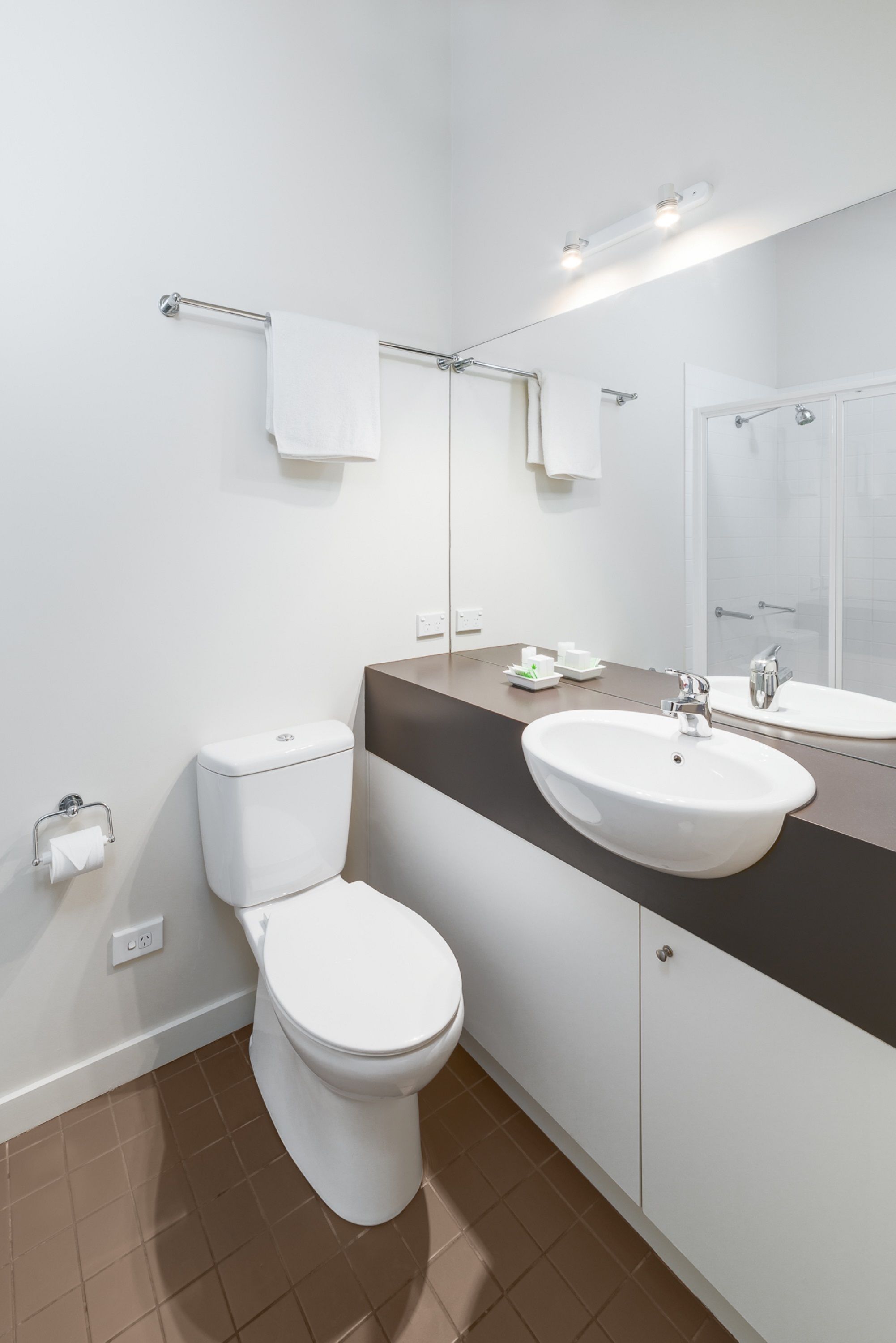 Une salle de bain moderne avec des toilettes blanches, un lavabo surmonté d’un miroir et un porte-serviettes fixé au mur.