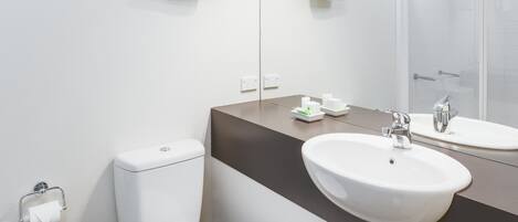 Une salle de bain moderne avec des toilettes blanches, un lavabo surmonté d’un miroir et un porte-serviettes fixé au mur.