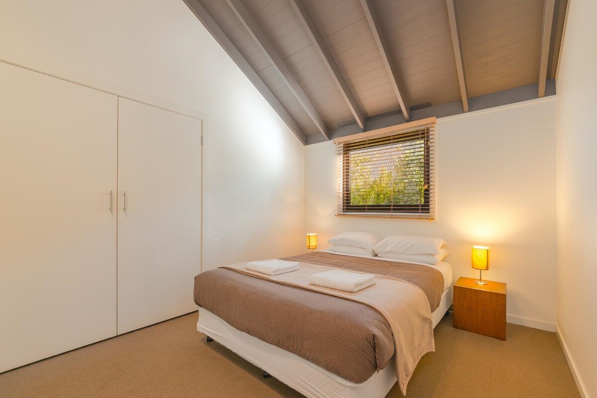 A bedroom with a bed, bedside lamps, a window with blinds, and a wardrobe.