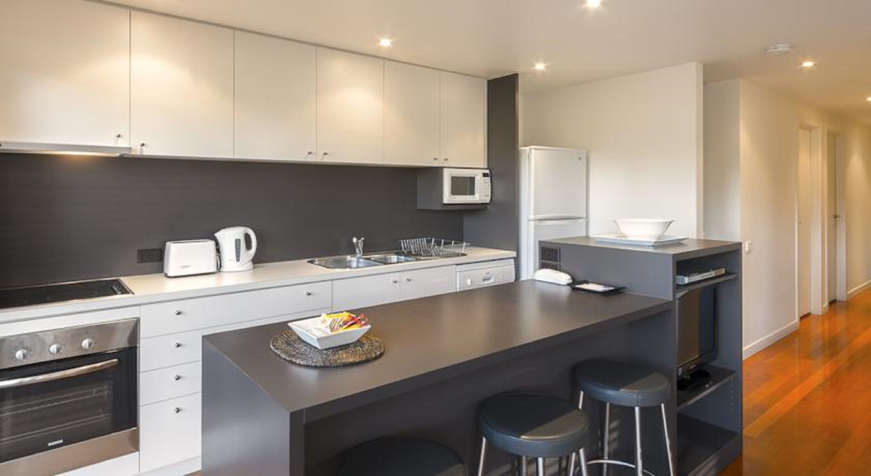 A modern kitchen with white cabinets, a black countertop, a microwave, a refrigerator, and a coffee maker. There are two bar stools at the island.
