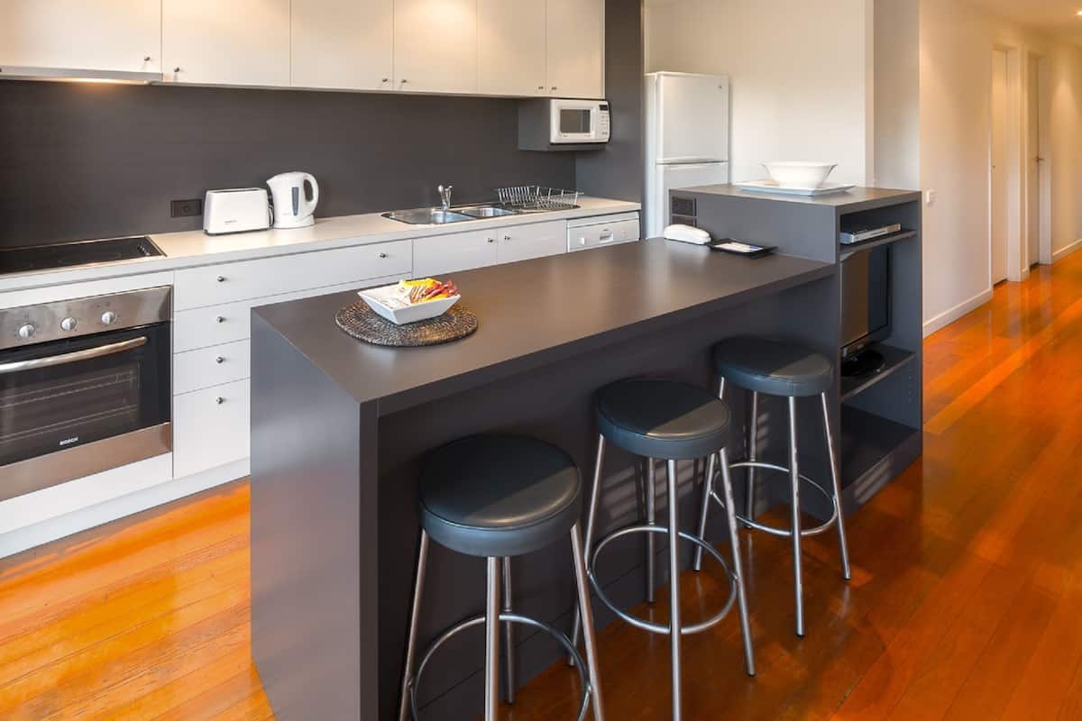Una cocina moderna con una isla central, taburetes de bar y electrodomésticos de acero inoxidable.