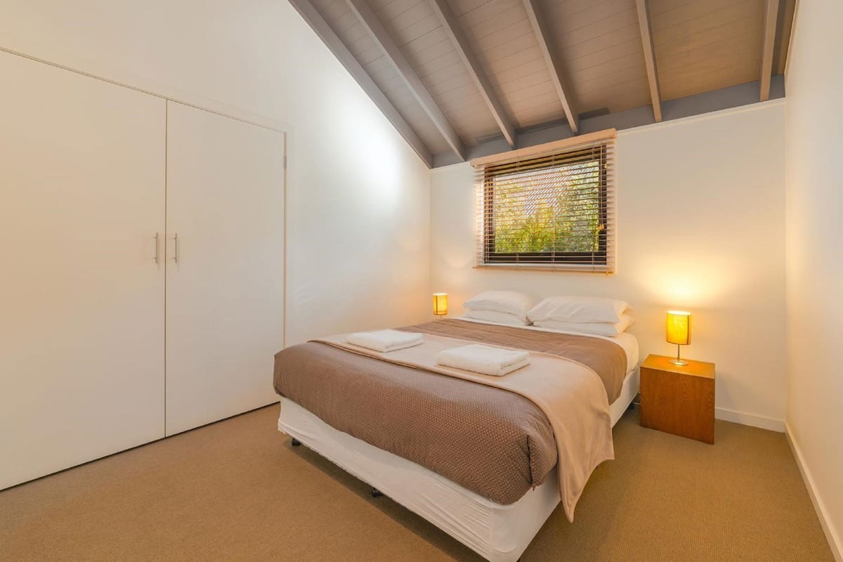 Un dormitorio con cama, lámparas de noche, una ventana con persianas y un armario.