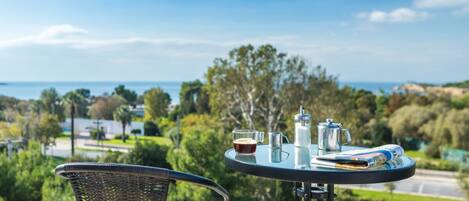 A table with a newspaper, a coffee pot, and a cup, set against a scenic view of a body of water and greenery.