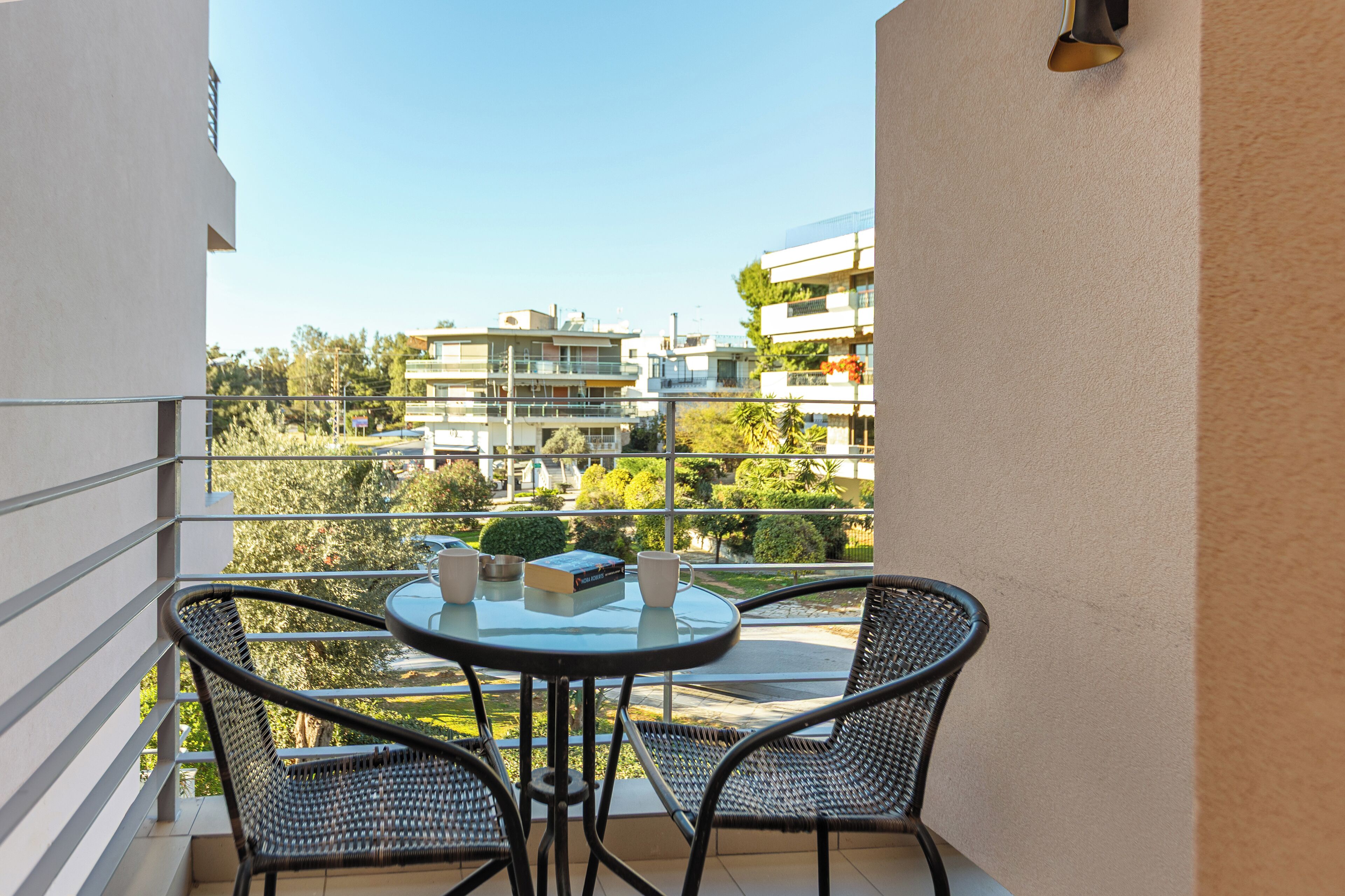 A balcony with a round table and two chairs, overlooking a residential area with modern buildings and greenery.