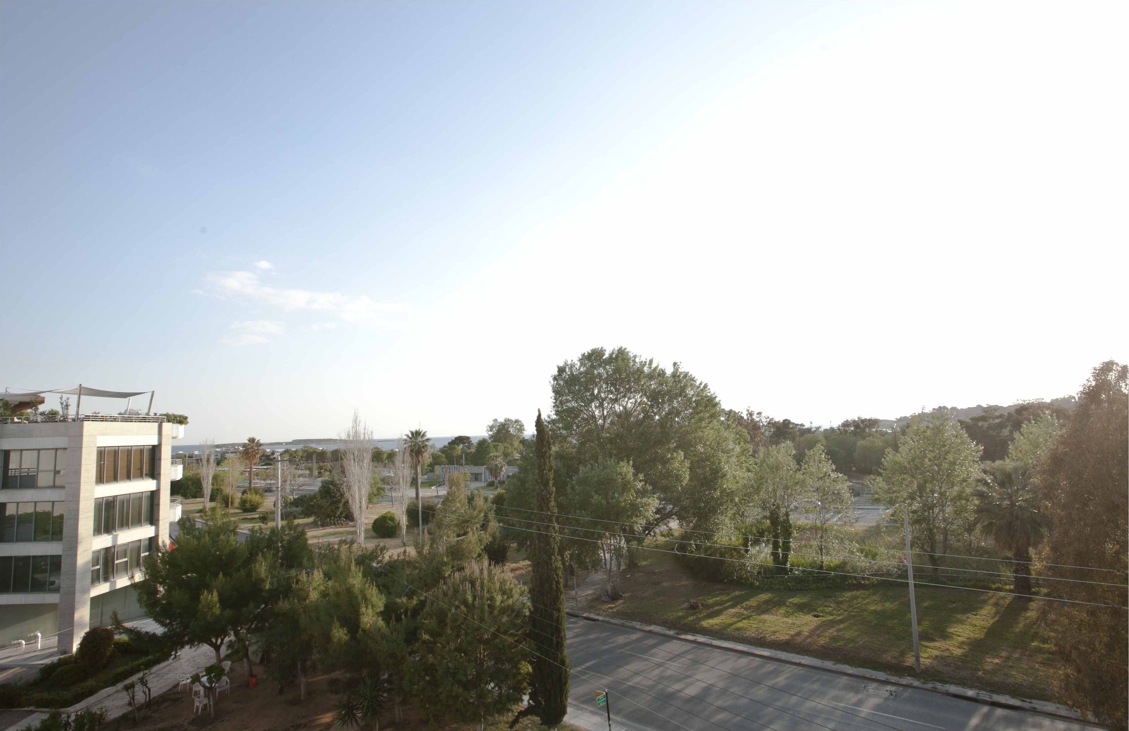 A multi-story building with a flat roof and a balcony, surrounded by trees and a clear sky.