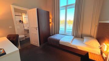A hotel room with a bed, a desk, a chair, a wardrobe, a bathroom, and a window with a view.