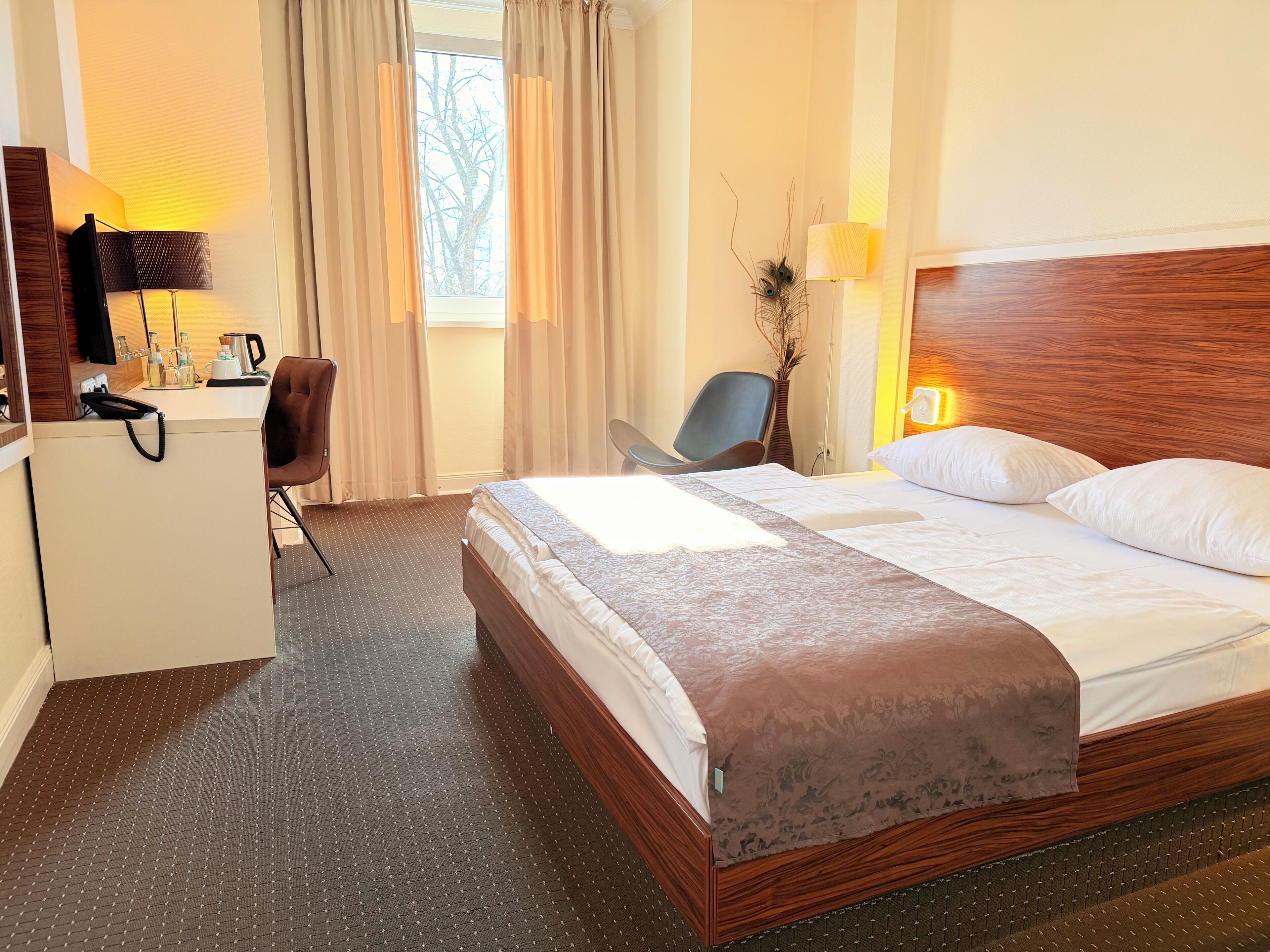 A hotel room with a bed, a desk with a telephone, a chair, and a lamp.
