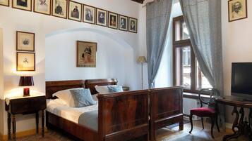 A bedroom with a wooden bed, a desk with a chair, a television, and a window with curtains.
