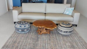A living room with a beige sofa, two patterned ottomans, and a brown furry stool.
