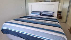 A modern bedroom with a large bed, a white headboard, and a mirrored closet.