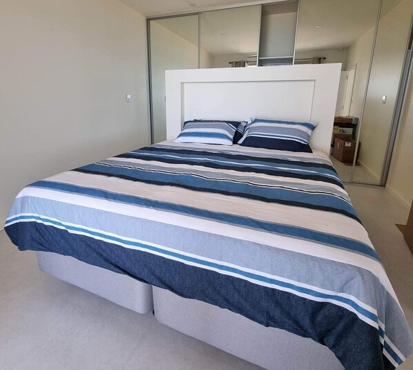 Une chambre moderne avec un grand lit, une tête de lit blanche et un placard avec des portes miroir.