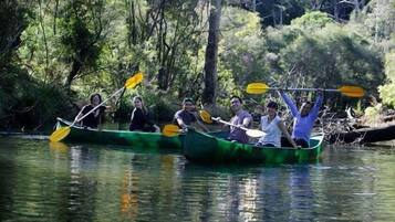 A group of people in a green canoe on a calm river surrounded by trees.