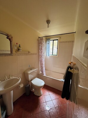 Un baño con inodoro, lavamanos, bañera y ventana con cortina.