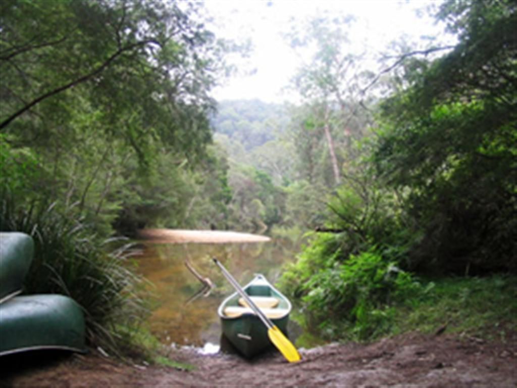 A canoe and a paddle by a muddy path in a forested area.
