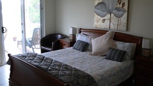Un dormitorio con cama, una silla, una mesita de noche y un cuadro en la pared.