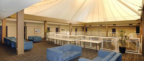A spacious indoor area with a high ceiling, blue seating, and a large tent-like structure.