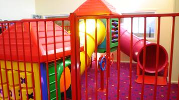 Un área de juegos con un tobogán rojo, estructuras para escalar amarillas y verdes, y un túnel rojo.