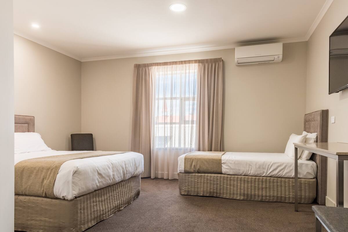Habitación de hotel con dos camas, un escritorio y una televisión.