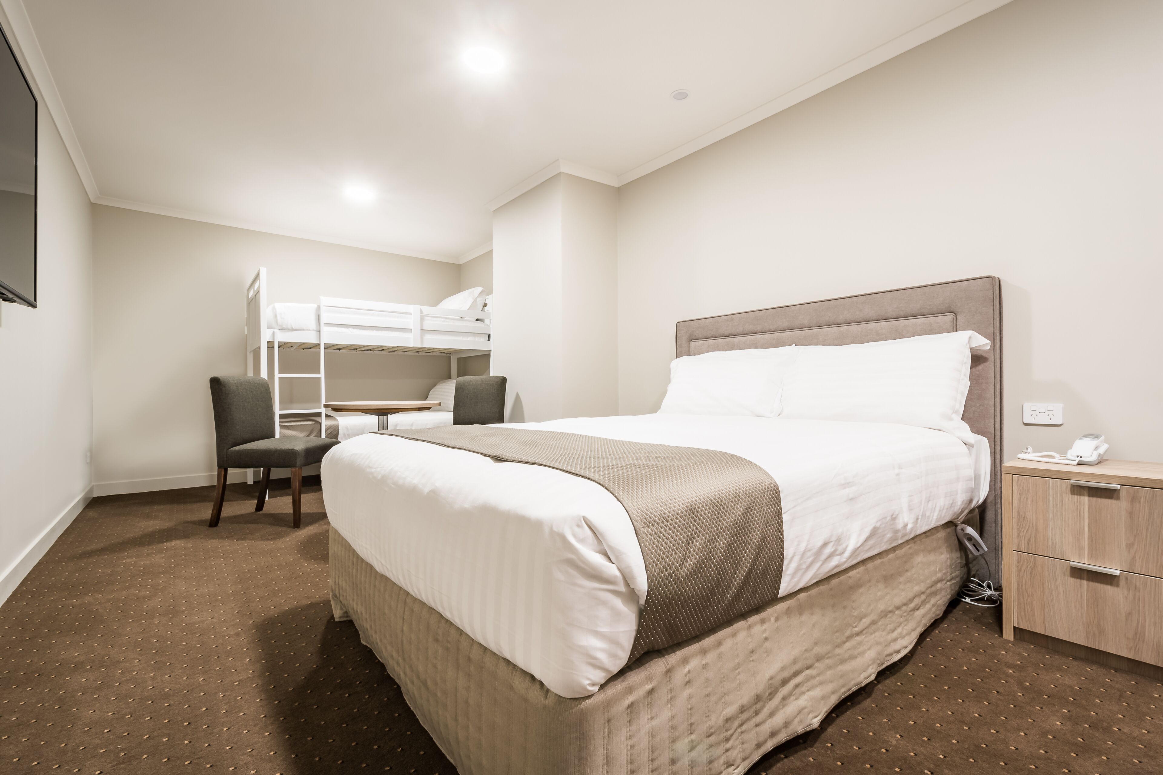 Quarto de hotel com uma cama grande, uma escrivaninha com cadeira, uma cama beliche e uma pequena mesa de cabeceira com telefone.