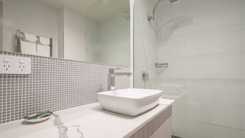 Un baño moderno con un lavamanos blanco, cabina de ducha con mampara de vidrio y salpicadero de azulejos.