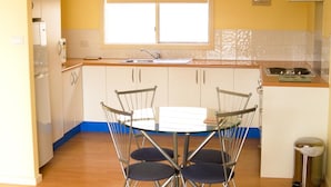 A compact kitchen with a round table and chairs, a window, and a stove. - Lindsays of Kangaroo Island (Penneshaw)