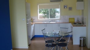 A compact kitchen with a window, a sink, a stove, and a dining area with chairs. - Lindsays of Kangaroo Island (Penneshaw)