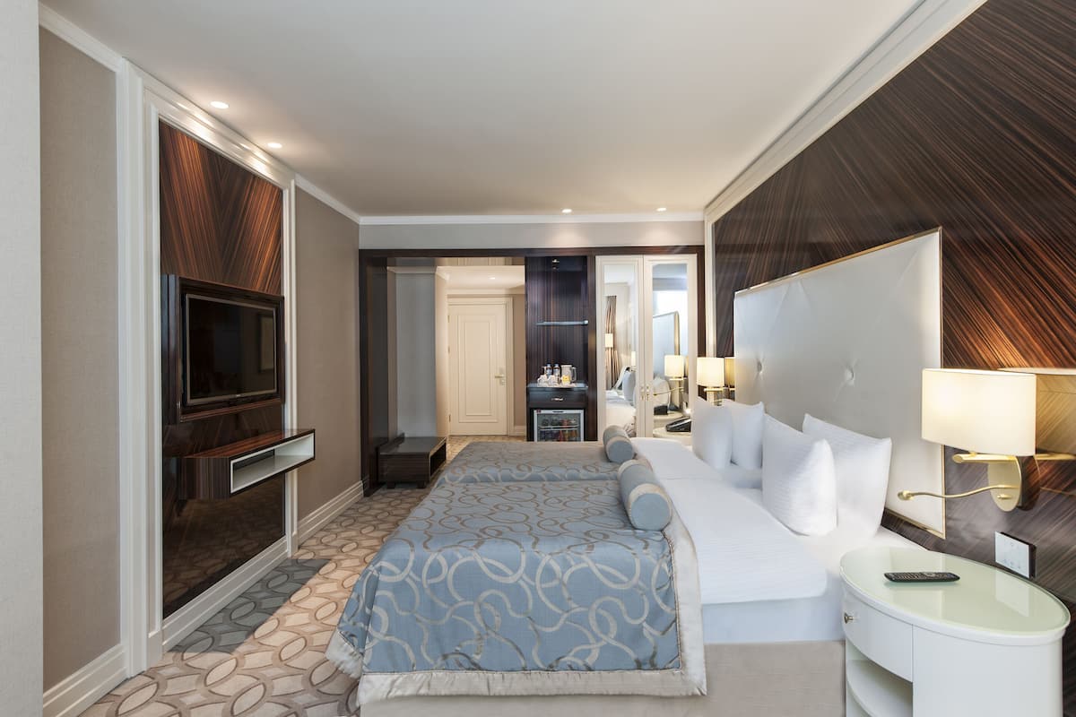 A modern hotel room with a large bed, a TV, a bedside table, and a mirror.