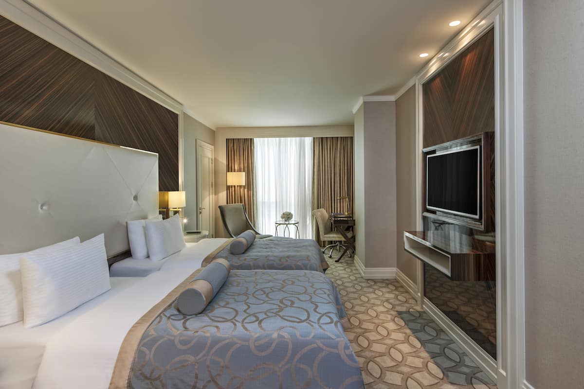 A hotel room with two beds, a TV, a desk, and a chair.
