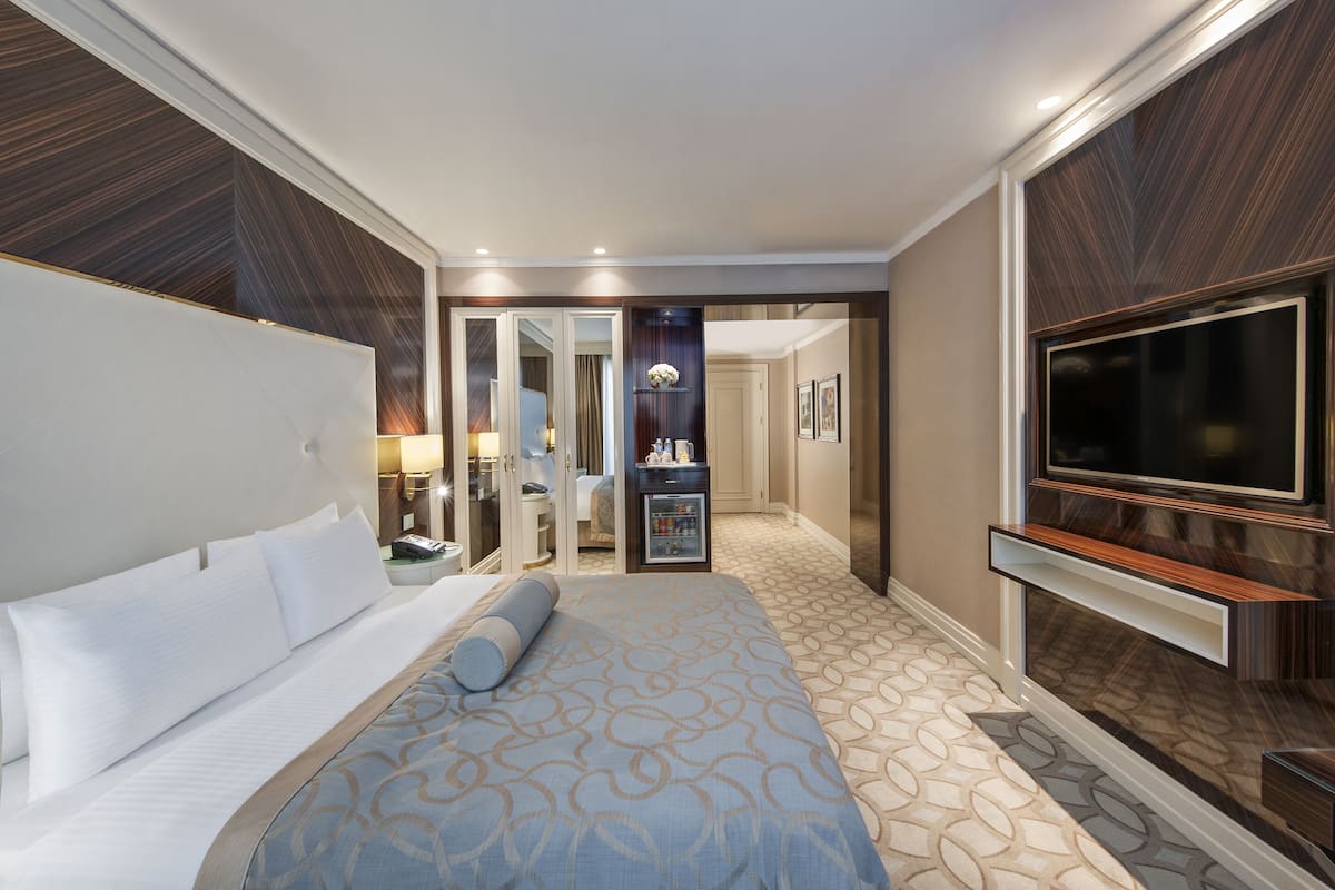 A hotel room with a large bed, a TV, a minibar, and a bathroom visible through an open door.