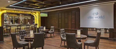 A bar area with leather chairs and tables, a television screen, and a banner reading "elite world business".