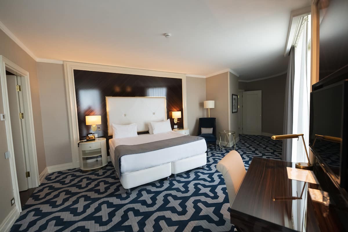 A hotel room with a large bed, bedside tables, a desk, and a TV.