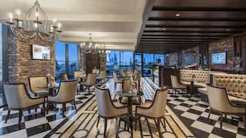 Un vestíbulo de hotel con piso a cuadros, mobiliario moderno, una zona de bar y grandes ventanales que ofrecen vistas al exterior.