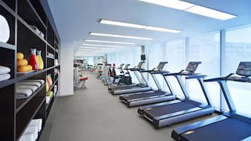 Une salle de sport équipée de tapis de course, d’appareils d’exercice et de serviettes rangées sur des étagères.