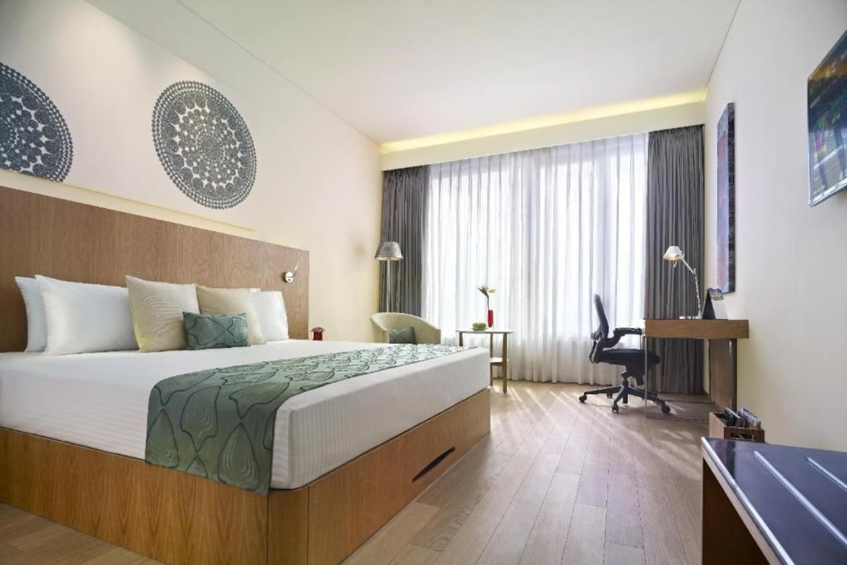 A hotel room with a bed, desk, chair, and curtains.