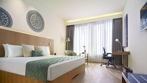 Quarto de hotel com uma cama grande, uma escrivaninha, uma cadeira e uma televisão.
