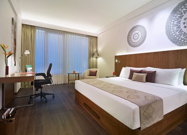 Une chambre d’hôtel avec un grand lit, un bureau avec une chaise, une petite table et une grande fenêtre avec des rideaux.