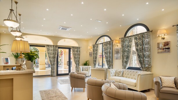 A spacious living area with a sofa, armchairs, and a coffee table. There are curtains, a lamp, and a plant.
